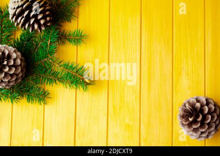 Cornice realizzata con rami di pino natalizio e coni su vecchia tavola di legno giallo. Spazio per il testo. Disposizione piatta Foto Stock