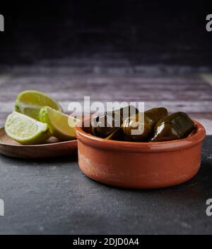 Dolma, foglie di vite ripiene in una ciotola di terracotta. Sarma in turco o Dolmades in cucina greca. Con lime a fette su un tavolo naturale. Foto Stock