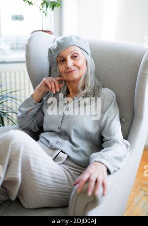 Ritratto di donna anziana con beretto grigio seduto all'interno su sfondo scuro. Foto Stock