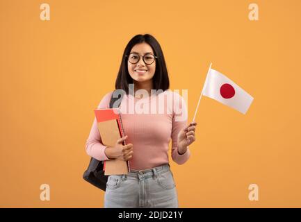 Studio linguistico e scambio di studenti. Sorriante giovane donna asiatica che tiene bandiera giapponese Foto Stock