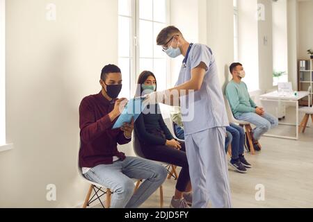 Giovane uomo firma carte che il medico gli dà prima di ricevere vaccino in clinica Foto Stock