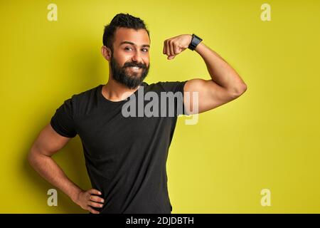 forte ragazzo arabico mostra muscoli braccia, godere di essere sportivo e forte, potente, sorrisi isolati su sfondo verde Foto Stock