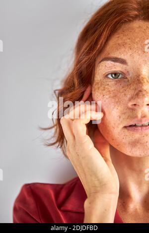 donna con testa rossa frettolosa che guarda la fotocamera, con uno sguardo serio e sicuro, tenendo le dita vicino al viso Foto Stock