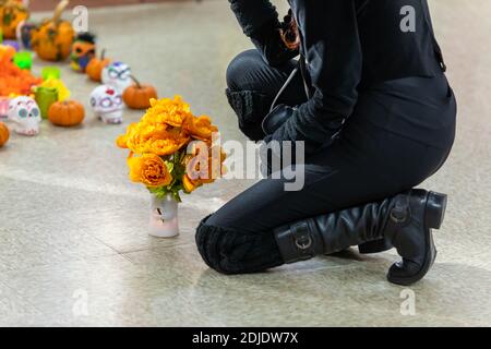 Fuoco selettivo della giovane donna in vestiti neri che si inginocchiano sopra pavimento con bouquet di campasuchil fresco durante il ricordo al dia de los muertos in Messico Foto Stock