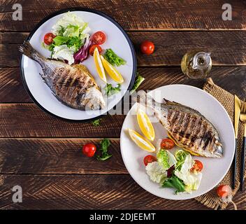 Delizioso dorado alla griglia o pesce orate con insalata, spezie, dorada alla griglia su un tavolo di legno. Vista dall'alto, in piano, in alto Foto Stock