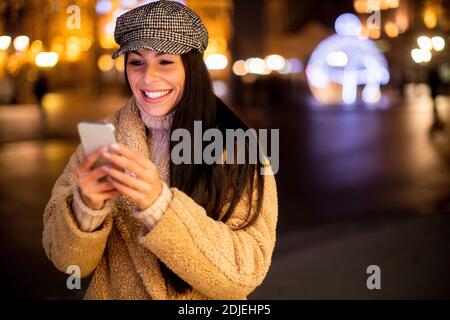 Bella giovane donna che usa il suo cellulare per strada A Natale Foto Stock