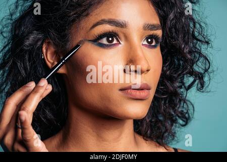 Foto di scorta di giovane donna ispanica che indossa trucco fresco utilizzando la spazzola per gli occhi e guardando al lato. Foto Stock