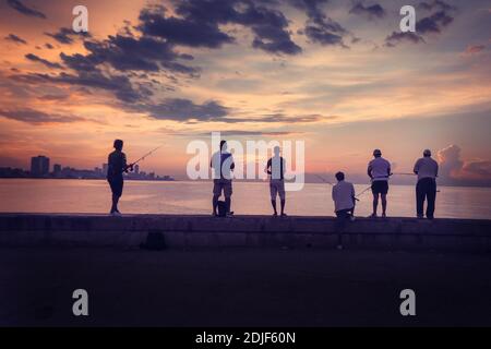 Cuban people are fishing in the ocean early morning during a sunny and cloudy sunrise, taken during the Shortage of Food Crisis. Stock Photo