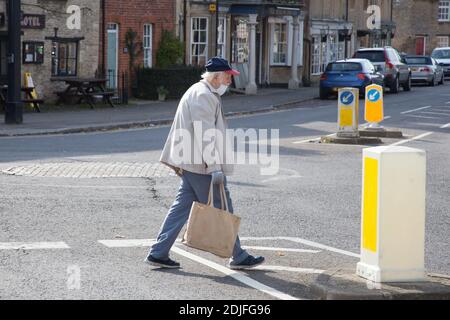 Un uomo anziano attraversa una strada a Bampton, Oxfordshire indossando una maschera facciale nel Regno Unito, preso il 19 ottobre 2020 Foto Stock