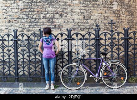 Giovane donna in maglia viola e viola vintage bicicletta sulla strada di Praga, Repubblica Ceca Foto Stock