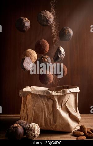 composizione fotografica creativa di deliziosi tartufi al cioccolato galleggiante e. borsa di carta artigianale su sfondo di legno Foto Stock