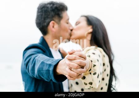 Coppia baciando le mani di tenuta con anello di fidanzamento di nozze che mostra con facce in primo piano di sfondo Foto Stock