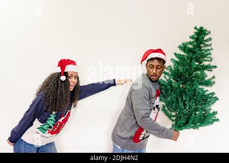 Coppia che corre con albero di Natale. Amici di Natale che indossano il cappello di santa tenendo albero di Natale. Sfondo bianco Foto Stock