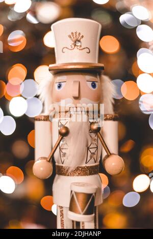 Statuetta frontale classico soldato batterista nutcracker con bianco e oro Uniforme e tamburo davanti all'albero di Natale sfocato con toni arancioni Foto Stock