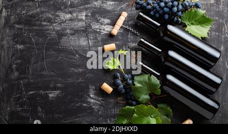 Bottiglie di vino, uva, grappoli d'uva con foglie e viti cavatappi di vino su fondo rustico scuro di calcestruzzo. Composizione di vino piatto con copia Foto Stock