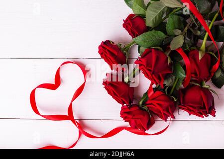 Concetto di giorno di San Valentino. Nastro rosso a forma di cuore, bouquet di rose e scatole regalo avvolte in papà kraft su tavolo di legno bianco. Foto Stock