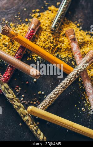 Un set di spezie in piccoli vasi con coperchi in sughero. Sale rosa, zenzero, curcuma, masala, paprika, paprika affumicata. Spezie su una superficie nera. Foto Stock