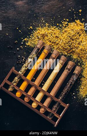 Un set di spezie in piccoli vasi con coperchi in sughero. Sale rosa, zenzero, curcuma, masala, paprika, paprika affumicata. Spezie su una superficie nera. Foto Stock