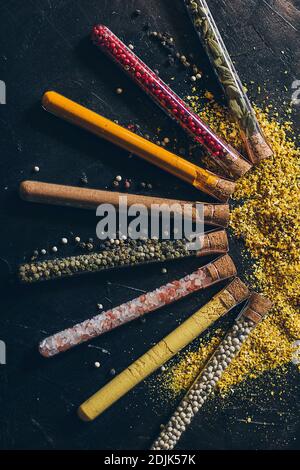 Un set di spezie in piccoli vasi con coperchi in sughero. Sale rosa, zenzero, curcuma, masala, paprika, paprika affumicata. Spezie su una superficie nera. Foto Stock