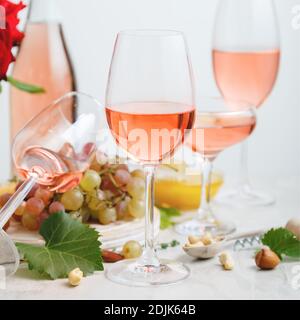 Vino rosato in diversi tipi di calici su fondo di cemento chiaro con uva. Composizione del vino con frutta a guscio e uva su tavola bianca. Ritaglio quadrato Foto Stock