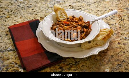 Ciotola di peperoncino con fagioli in un recipiente bianco con pane sul lato. Foto Stock