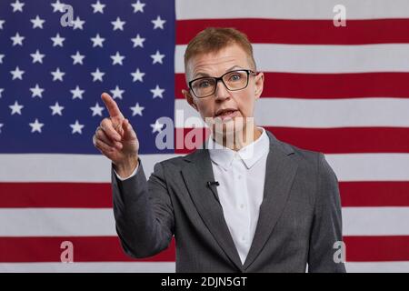 Vista frontale ritratto di donna matura politico dando voce e gesturing mentre si sta in piedi contro USA bandiera sfondo, copia spazio Foto Stock