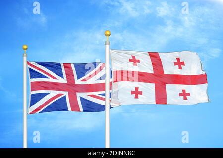 Regno Unito e Georgia due bandiere su flagpoli e blu cielo nuvoloso Foto Stock