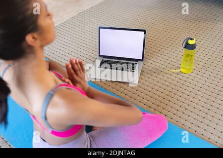 Donna di razza mista che pratica yoga a casa utilizzando il suo computer portatile Foto Stock