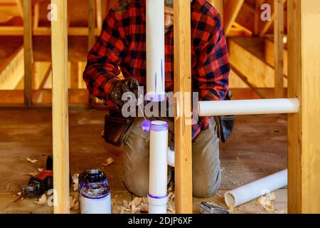 Idraulico applicazione di colla su un tubo di scarico in PVC nell'area di lavoro. Foto Stock