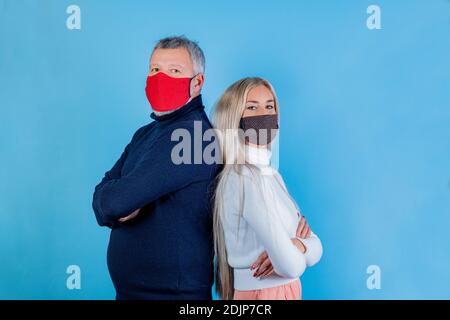 Ritratto di hipster uomo e giovane ragazza in piedi schiena con braccia ripiegate che indossano mascherine colorate isolate sfondo blu chiaro Foto Stock