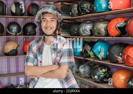 uomo sorridente che indossa il casco con le mani incrociate sul display del casco sfondo rack Foto Stock