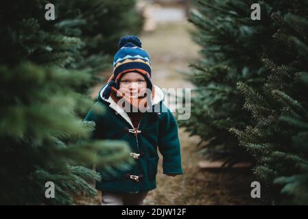 Adorabile bambino che indossa un cappotto di lana che cammina tra gli alberi di natale Foto Stock