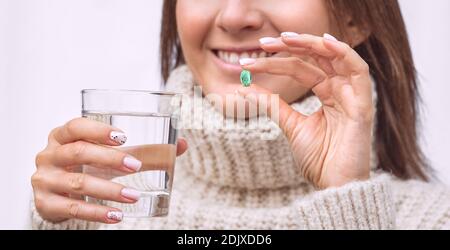 Donna sorridente felice che tiene un bicchiere d'acqua e prende capsula con vitamine Foto Stock