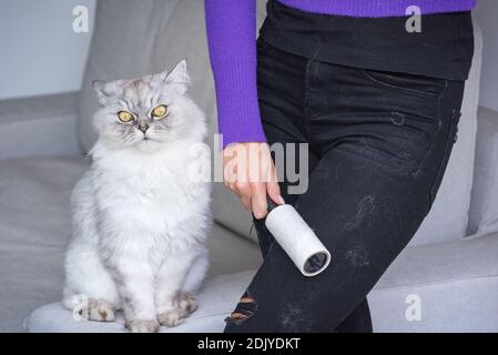 Donna che pulisce i vestiti con il rullo di pelucchi o il rullo adesivo da gatti capelli Foto Stock