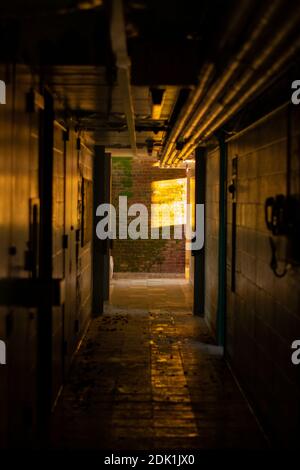 Un corridoio scuro all'interno di un Dormitorio abbandonato con luce arancione Alla fine di esso Foto Stock