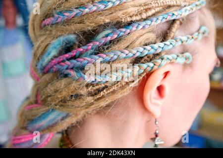 Dreadlock e pigtail colorati sulla testa luminosa della ragazza. Vista laterale, nessuna faccia visibile. Foto Stock