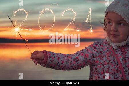 Bella ragazza scritta con sparkle fuochi d'artificio su sfondo tramonto, felice anno nuovo 2021 concetto. Foto Stock