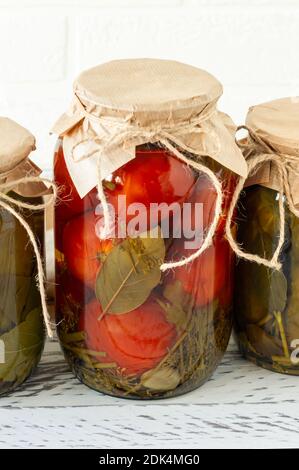 Pomodori e cetrioli fatti in casa conserve in vaso di vetro su sfondo di legno. Foto Stock