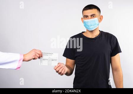 Un uomo in maschera medica riceve una scheda di vaccinazione da un medico. Concetto di coronavirus. Decisione sicura Foto Stock