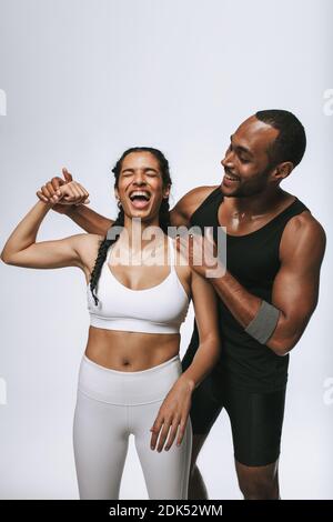 Amici che si divertono in palestra. Donna felice in forma fisica indossare mostrando il suo bicipite con il suo amico maschio dal suo lato. Foto Stock