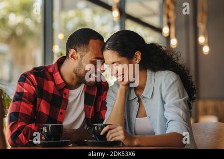 Una coppia romantica che si gode di stare insieme in un caffè. Uomo e donna africani seduti al tavolo della caffetteria che parla e sorride. Foto Stock