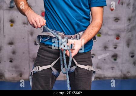 Primo piano dell'arrampicatore con attrezzatura da arrampicata, nodo di legatura su imbracatura di sicurezza, preparazione per l'arrampicata. Dettagli persona non riconoscibile. Foto Stock