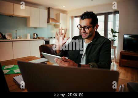 Un uomo d'affari da corsa misto che si sventolerà al tablet digitale mentre interagirà videochiamata con i clienti Foto Stock