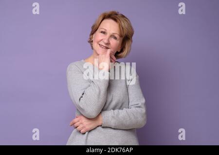 Donna anziana che sorride alla telecamera con la mano sul mento. Scatto in studio Foto Stock