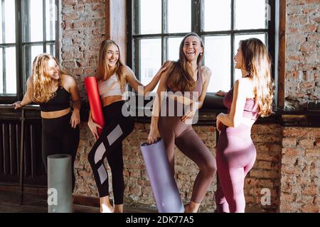 Un gruppo di quattro giovani donne parla dopo la lezione di yoga monolocale in stile loft chiaro e sorriso Foto Stock