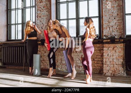 Un gruppo di quattro giovani donne parla dopo la lezione di yoga monolocale in stile loft chiaro e sorriso Foto Stock