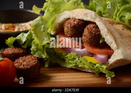 Falafel in pita pane con insalata di verdure, salsa harissa, humus, tahini su fondo di legno. Concetto di fast food mediorientale. Tradizionale israeliano f Foto Stock