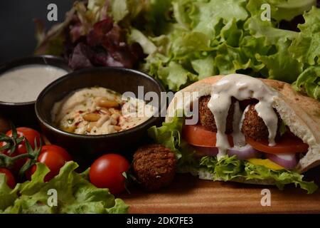 Falafel in pita pane con insalata di verdure, salsa harissa, humus, tahini su fondo di legno. Concetto di fast food mediorientale. Tradizionale israeliano f Foto Stock