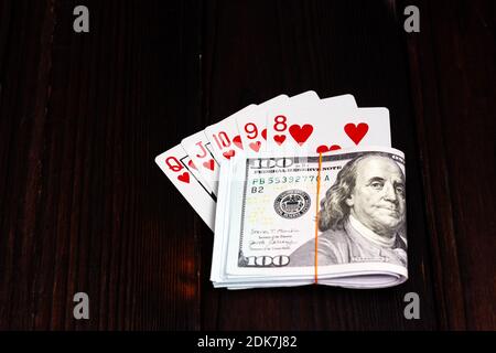 Un pacchetto di dollari legato con una fascia elastica e una combinazione di carte da gioco su un tavolo di legno scuro. Fortunata vittoria, jackpot. Royal Flush nel poker. Foto Stock