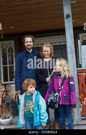 Genitori con due bambini in piedi di fronte alla casa Foto Stock